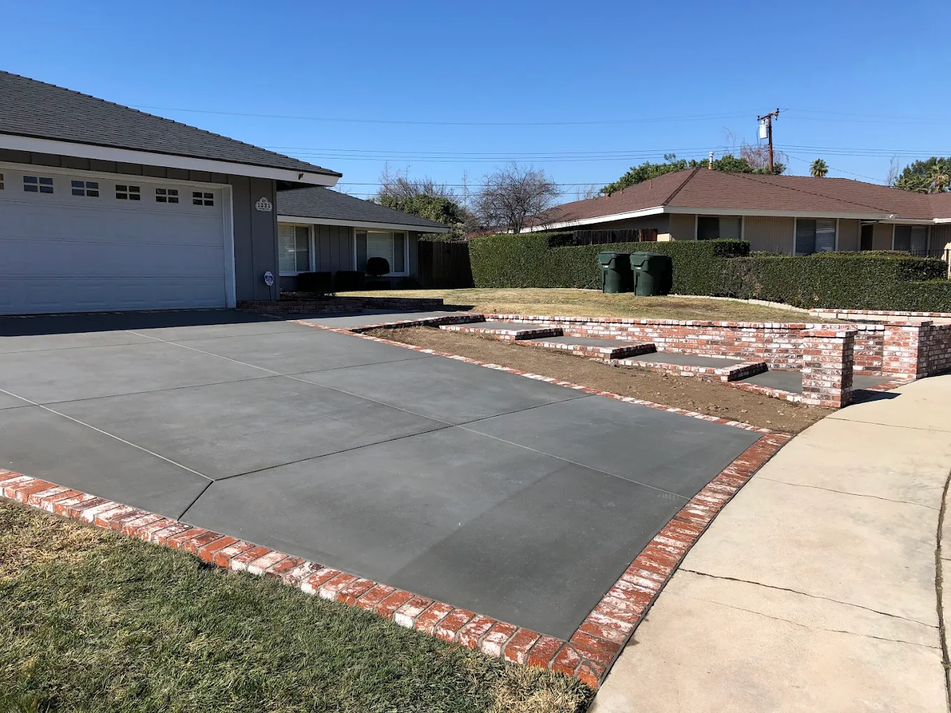 A fresh concrete driveway with a brick border and low brick wall
